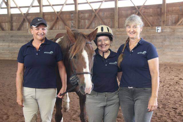 Elaine Copy Judith & me with CH shirts 3 smiling women standing with a chestnut horse with a white blaze in a riding arena