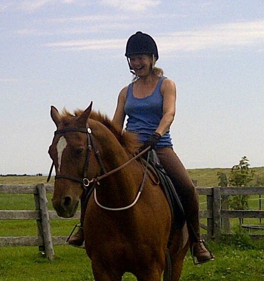 Jackie and Stitch smile Woman smiling with joy riding a chestnut horse with a white blaze